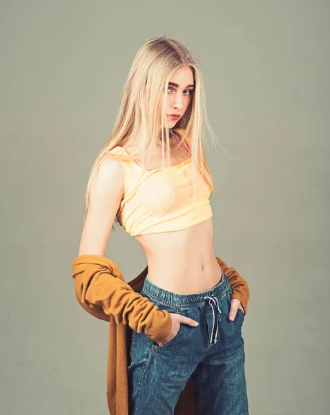 Blond model in yellow top and boyfriend style jeans posing with her hands in pockets isolated on gray background — Stock Photo, Image