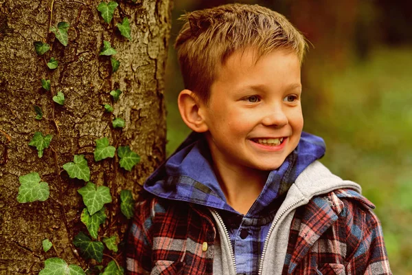Mantenham-se positivos e felizes. Desfrute de jogos de infância. Rapaz feliz a sorrir para a árvore. Menino com um sorriso adorável. Seja feliz por este momento, este momento é a sua vida de infância — Fotografia de Stock
