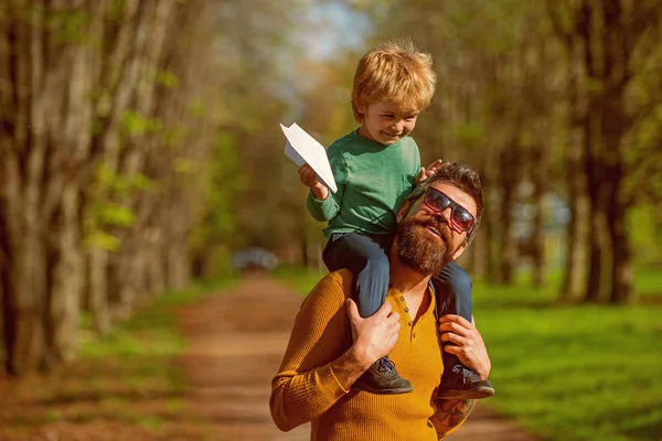 Viajando en avión. Niño pequeño en el hombro de los padres lanzamiento avión de papel en el parque, concepto de viaje. Volar mejor que nunca — Foto de Stock