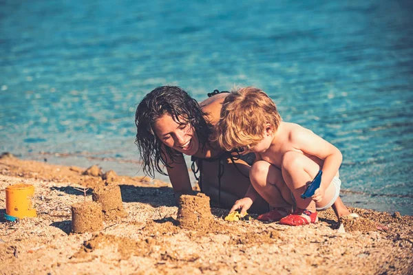 Мать с сыном строят песчаный замок в море. Счастливая семья на Карибском море. Летние каникулы и путешествие в океан. Мальдивы или пляжные развлечения Майами. День матери праздник мальчика и женщины родителя . — стоковое фото