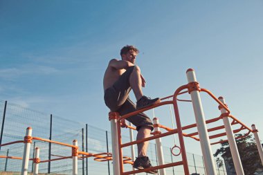 Adam atlet tırmanmaya üzerinde metal oyuncağınızda mavi gökyüzü. Sporcu demirlere üstte çıplak gövde ile. Maço egzersiz yaptıktan sonra açık sakin ol. Spor Sağlık ve enerji kavramı