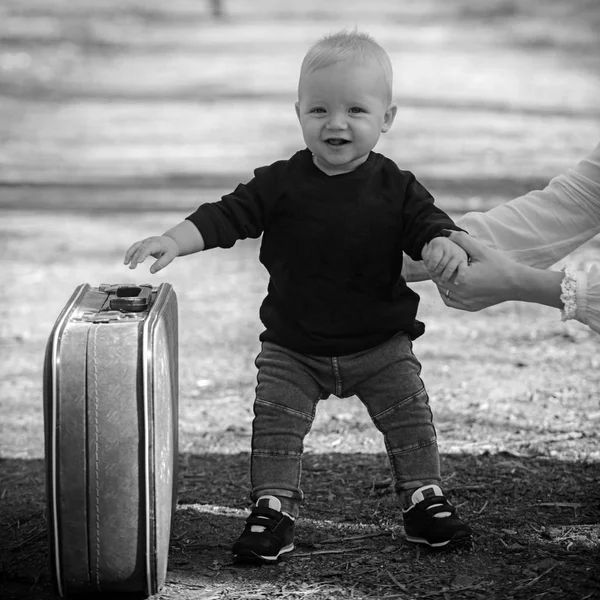 Мальчик несет чемодан по природному пейзажу. Мальчик путешествует в отпуск с ретро-сумкой с материнской рукой — стоковое фото