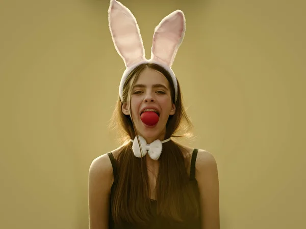 Chica de Pascua sosteniendo huevo rojo en la boca sobre fondo beige —  Fotos de Stock