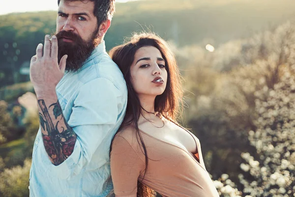 Pareja en caras relajadas fumando al aire libre, naturaleza en el fondo, desenfocado. Concepto de hábito de fumar. Hombre y mujer sostienen el cigarrillo en el día de primavera. Pareja enamorada pasar tiempo al aire libre y fumar . —  Fotos de Stock