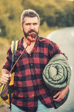Kasabaya geri yolda otostopçu. Sırt çantası, uyku geri sopa sosis yeme sakallı adam. Ormanda hiking yaz