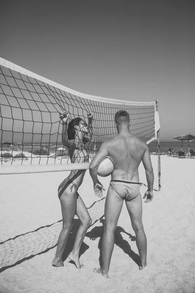 カップルは楽しくバレーボールをプレーします。スポーティなアクティブなカップルはバレーボール ・ ネットの近くに立つ、夏の日のゲームをプレイします。女と男フィット、強く、健康なビーチでスポーツを行います。ビーチ バレーボール コンセプト. — ストック写真