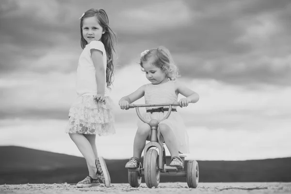 Chica paseo en triciclo con hermana en el cielo nublado —  Fotos de Stock