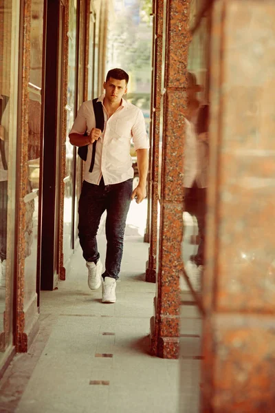 Handsome guy with backpack on vacation. Man with travel bag on sunny outdoor, wanderlust. Macho in fashionable shirt and jeans. Fashion model on street. Youth style concept — Stock Photo, Image