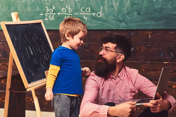 Otec a syn v učebně. Boční pohled muž a dítě na sebe dívali s pobavením. Chlap v růžové košili na podlaze s notebookem — Stock fotografie