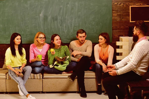 College and university concept. Group of students, group mates listening teacher, lecturer, professor. Students, scientists studying , professor holds laptop, teaches, explains, chalkboard background