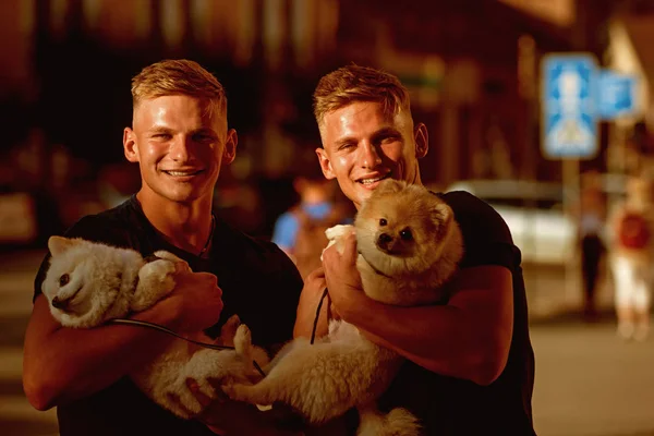 Dogs bring them joy. Muscular men with dog pets. Happy twins with muscular look. Twins men hold pedigree dogs. Spitz dogs love the company of their family. Happy family on walk