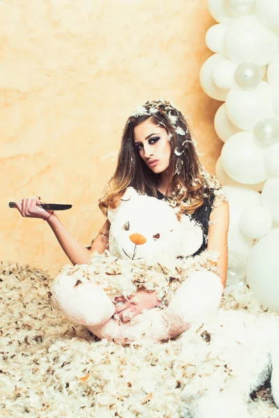 Чувственная женщина и кукла-животное в перьях снежинки. Женщина режет плюшевого мишку ножом. Подарок на Рождество, Новый год или день рождения. Концепция плохого поведения и агрессии — стоковое фото