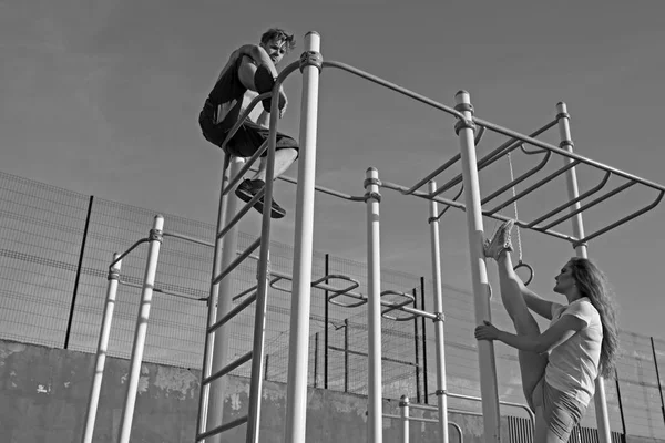 Sport paar opleiding in metalen jungle gym. Man atleet klimmen op boven- en vrouw split been. Sportman en Sportvrouw van monkey bars. Sport, training en pilates concept — Stockfoto