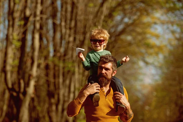 Niño jugando con avión de papel en el hombro del padre en el parque. Padre e hijo jugando juntos al aire libre. Es hora de volar — Foto de Stock