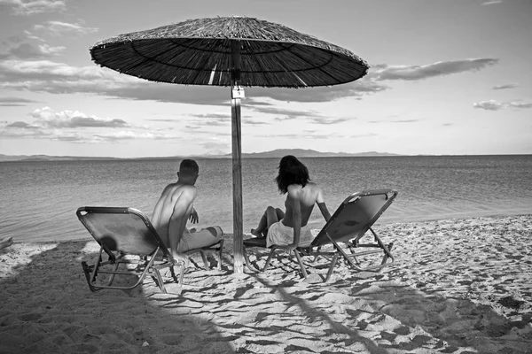 Relaciones amorosas de pareja desnuda en el mar. Familia y día de San Valentín. Pareja enamorada de cuerpo sexy relajarse en la playa. Vacaciones de verano y vacaciones de viaje paraíso. Mujer sexy y hombre bronceado en el paraguas . — Foto de Stock