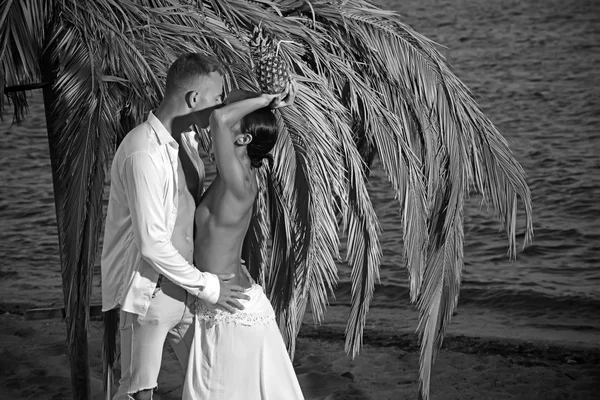 Happy kyssar par i vitt. tropiska solnedgången med palmträd och ananas. — Stockfoto