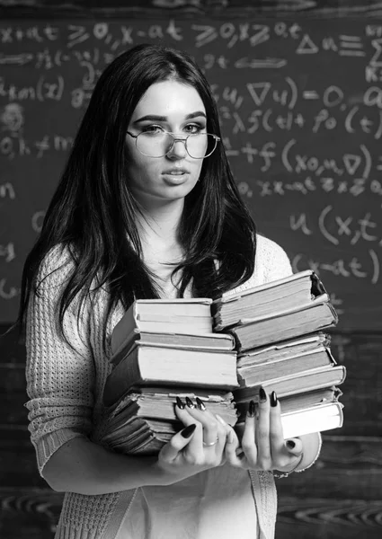 Lovely female student with heap of books standing in classroom. Brunette college girl cramming before exams