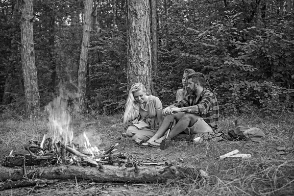 Active lifestyle concept. Group of friends camping in the forest. Girl reading next to bonfire