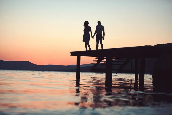 Silhouette coppia crepuscolo sul molo in acqua di mare. tramonto coppia silhouette passeggiata al tramonto località balneare . — Foto Stock