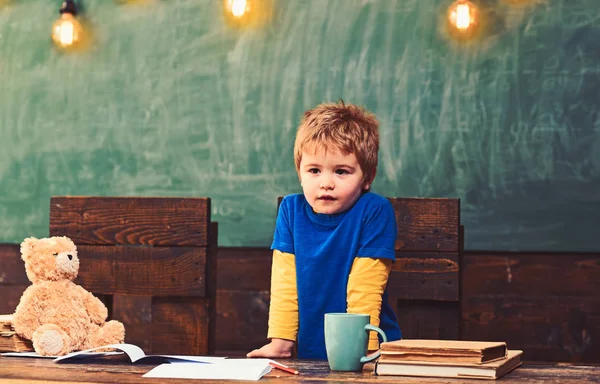 Μικρό αγόρι με σοβαρό πρόσωπο στέκεται πίσω από το σκοτεινό ξύλινο τραπέζι. Συμπυκνωμένο παιδί ακουμπισμένο στο τραπέζι. Παιδί που προσποιείται να είναι δάσκαλος — Φωτογραφία Αρχείου