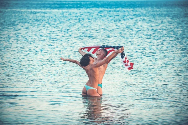 Bandera americana en el agua con la mujer sexy y el hombre, el día de la independencia. bandera americana como símbolo usa a sexy pareja en agua de mar . — Foto de Stock