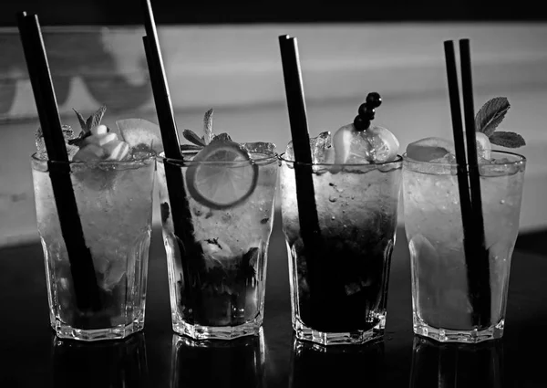 Полная мера прутьев. Коктейльные напитки подаются в стаканах с соломинками. Ледяные напитки в коктейльных бокалах. Алкогольные напитки со льдом. Сочные напитки с алкоголем на столе. Алкогольная зависимость — стоковое фото