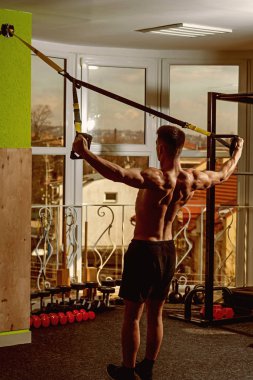 Spor ve spor salonu konsept. Gövde, sporcu, atlet, kas maço mu egzersiz trx döngüler ile pencere arka plan üzerinde olan adam. Adam çıplak gövde ve geri içinde jimnastik salonu kas eğitim, trx zevk.