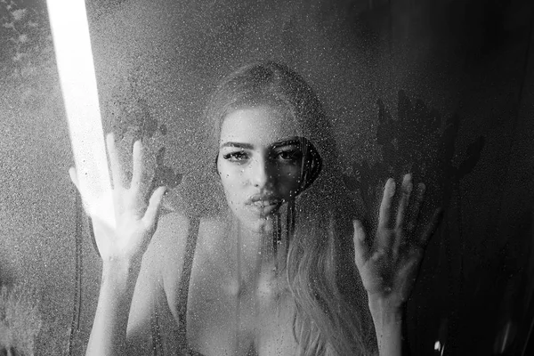 Fashion beauty and love. Window with water drops before girl with makeup. Sexy woman behind plastic sheet with water drops. Rain drops on window glass in heart shape. Shower and hygiene spa treatment