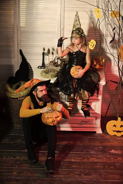 Wizard and witch in hats carve pumpkins. Father and daughter