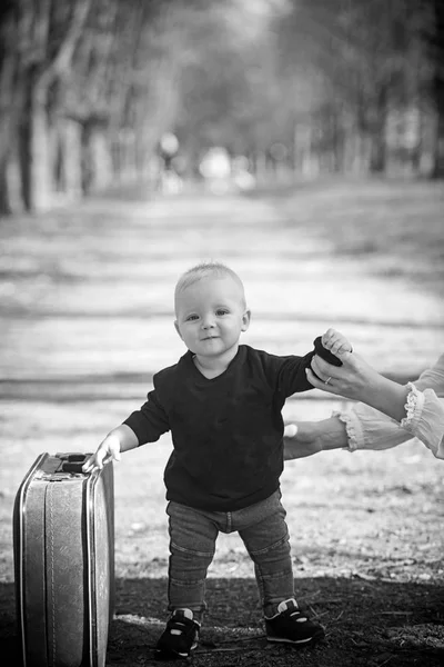 Ребенок путешествует с багажом на открытом воздухе. Маленький мальчик носит ретро чемодан на природном ландшафте. Детские поездки на отдых с сумкой с маминой рукой. Путешествия в отпуск и похоть — стоковое фото