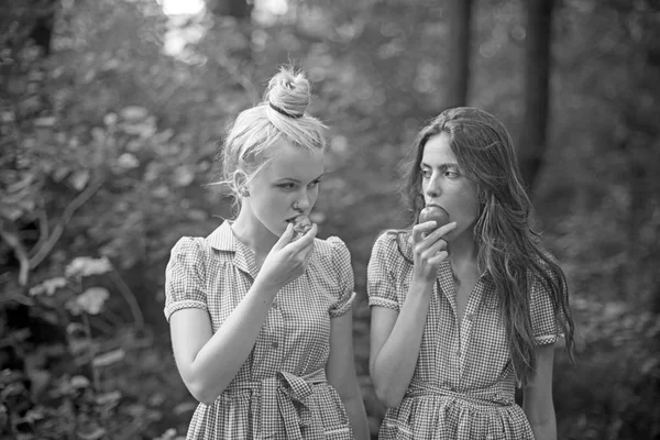 Camping in woods. Beautiful young girls wandering in forest. Two sisters in vintage dresses eating juicy tomatoes. Vitamins, nutrition and healthy diet concept
