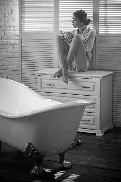 Mulher de moda em casaco no banho. Mulher senta-se na gaveta da casa de banho. Menina beleza comer comida de tigela. Dieta para saúde e cuidados de saúde — Fotografia de Stock