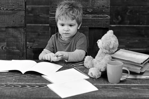 Tillbaka till skolan. Barn tittar på copybooks på träbord. Liten koncentrerad pojke håller färgglada pennor — Stockfoto