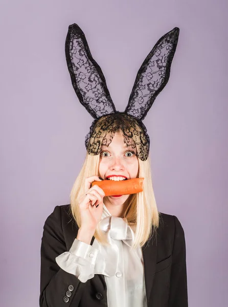 Mujer conejita sorprendida usando orejas de conejo y comer zanahoria. Feliz Pascua y divertido día de Pascua. Sonríe pascua. — Foto de Stock