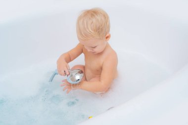 Çocuk bebek beyaz küvette banyo almak. Banyoda bir çocuk. Köpük banyosu içinde mutlu bebek yüz. Banyoda ve oyuncakları ile oynarken mutlu bebek.