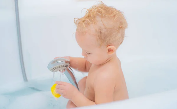 1 årig baby badar i dusch. Isolerade på vit bakgrund med urklippsbana. Rolig blont barn pojke att ha kul med vatten genom att ta bad i badkar. — Stockfoto