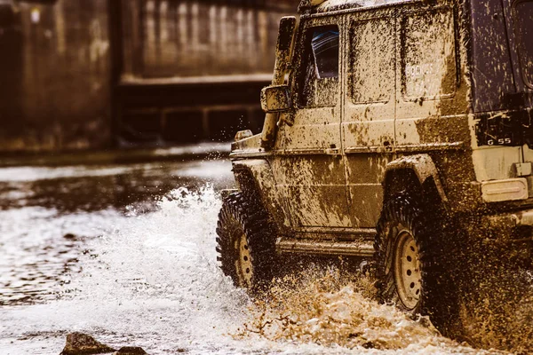 Schlamm und Wasser plätschern im Gelände. Blick von unten auf großes Offroad-Autorad auf Landstraße und Bergkulisse. Geländewagen fährt auf den Berg. — Stockfoto