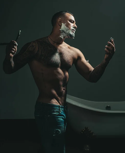 Kappers werken voor een knappe vent in de kapperszaak. Man die een kapper bezoekt in de kapperszaak. Baard balsem. Scheerman en scheermes man. Barbier scheert een man met baard in een kapperszaak. — Stockfoto