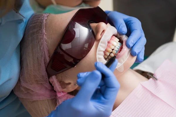 Dentiste guérir une patiente au cabinet dentaire dans un environnement agréable. Jeune femme blonde ouvrant la bouche alors qu'un dentiste non identifiable en gants de latex vérifie l'état de ses dents . — Photo