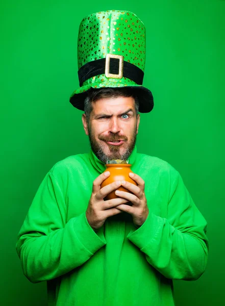Человек в день Святого Патрика лепрекон шляпа партии держать горшок золота на зеленом фоне. Happy St. Patricks Day concept with pot of gold . — стоковое фото