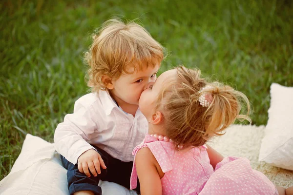 Девушка целует мальчика с светлыми волосами на зеленой траве — стоковое фото