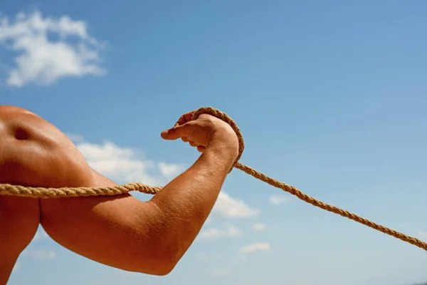 Gaining muscle. Sport training. Strong arm and shoulders tugging rope. Test of muscular strength. Physical strength and muscular power. Sport and fitness. Male muscular hand pulling rope