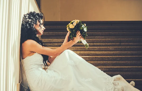Nevěsta v bílé šaty. Smyslná žena s svatební kytice. Žena s květinami sedět na schodiště. Dívka s svatební líčení a účes. Svatba a čeká na budoucnost. — Stock fotografie