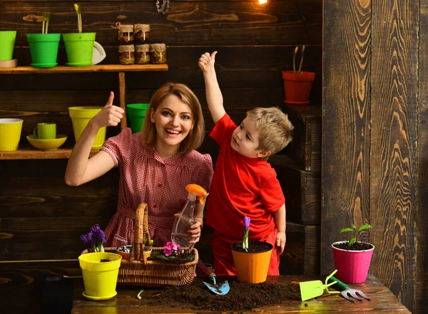 Flower concept. Happy family smile with thumbs up in flower shop. Mother and little son plant flower in pot. Every flower is a soul blossoming in nature