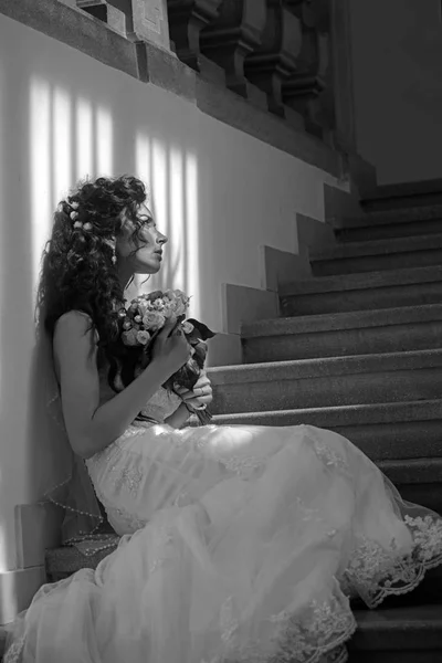 ブライダルのメイクや髪型を持つ少女。結婚式のブーケとの官能的な女性。花を持つ女性は、階段に座っています。花嫁の白のファッションのドレス。結婚式や未来を待っています。 — ストック写真