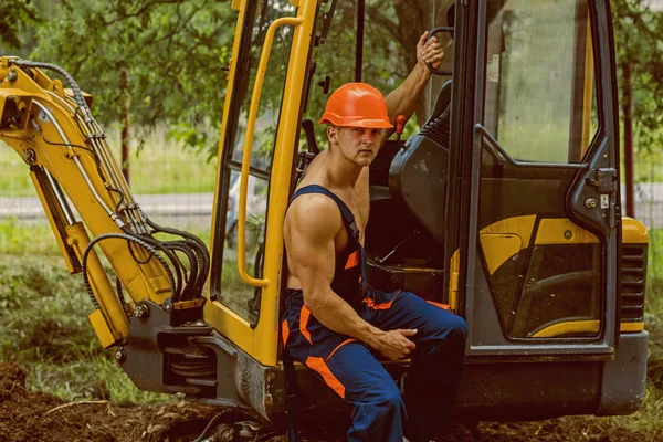 Driver concept. Excavator driver on construction site. Man driver at digger cabin. Muscular driver in working uniform