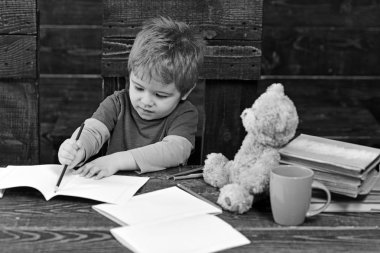 Çocuk çizim satırı mavi kalemle yoğunlaşmıştır. Meşgul çocuk egzersiz yazarak. Öğrenci ahşap paneller arka plan üzerinde