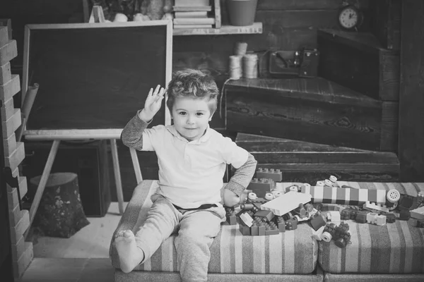 Barndomen koncept. Pojke leker med Bygg klossar i lekrummet nära svarta tavlan. Barfota barn sitter på soffan med färgglada plast block — Stockfoto