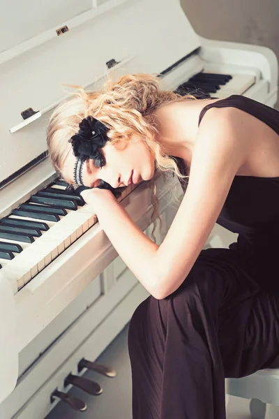 Красивая блондинка в повязке лежала на клавиатуре белого фортепиано с закрытыми глазами. Назад в 1920-е годы — стоковое фото