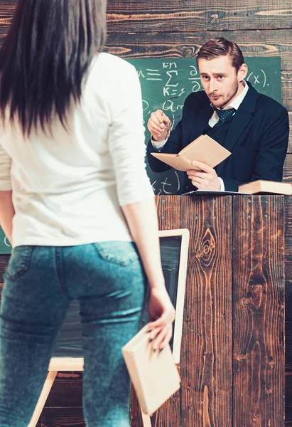 Girare indietro bruna ragazza tenendo libro in mano. rigoroso insegnante guardando la sua femmina studente mentre in piedi a rostrum . — Foto Stock